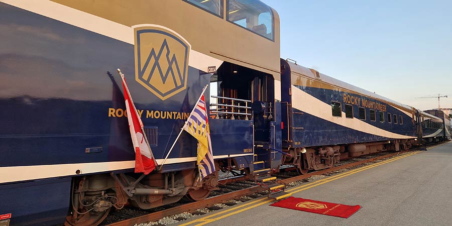 The Rocky Mountaineer train waiting at the platform, it is decorated with the Canadian flag and a Rocky Mountaineer branded red carpet to welcome guests aboard. 